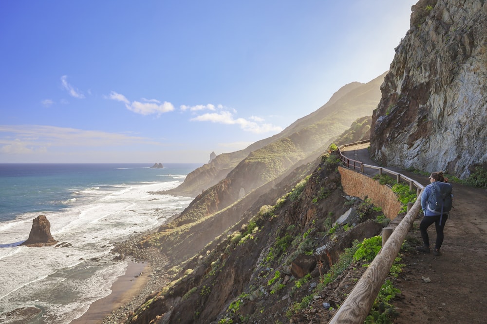 a man walking down a path next to the ocean