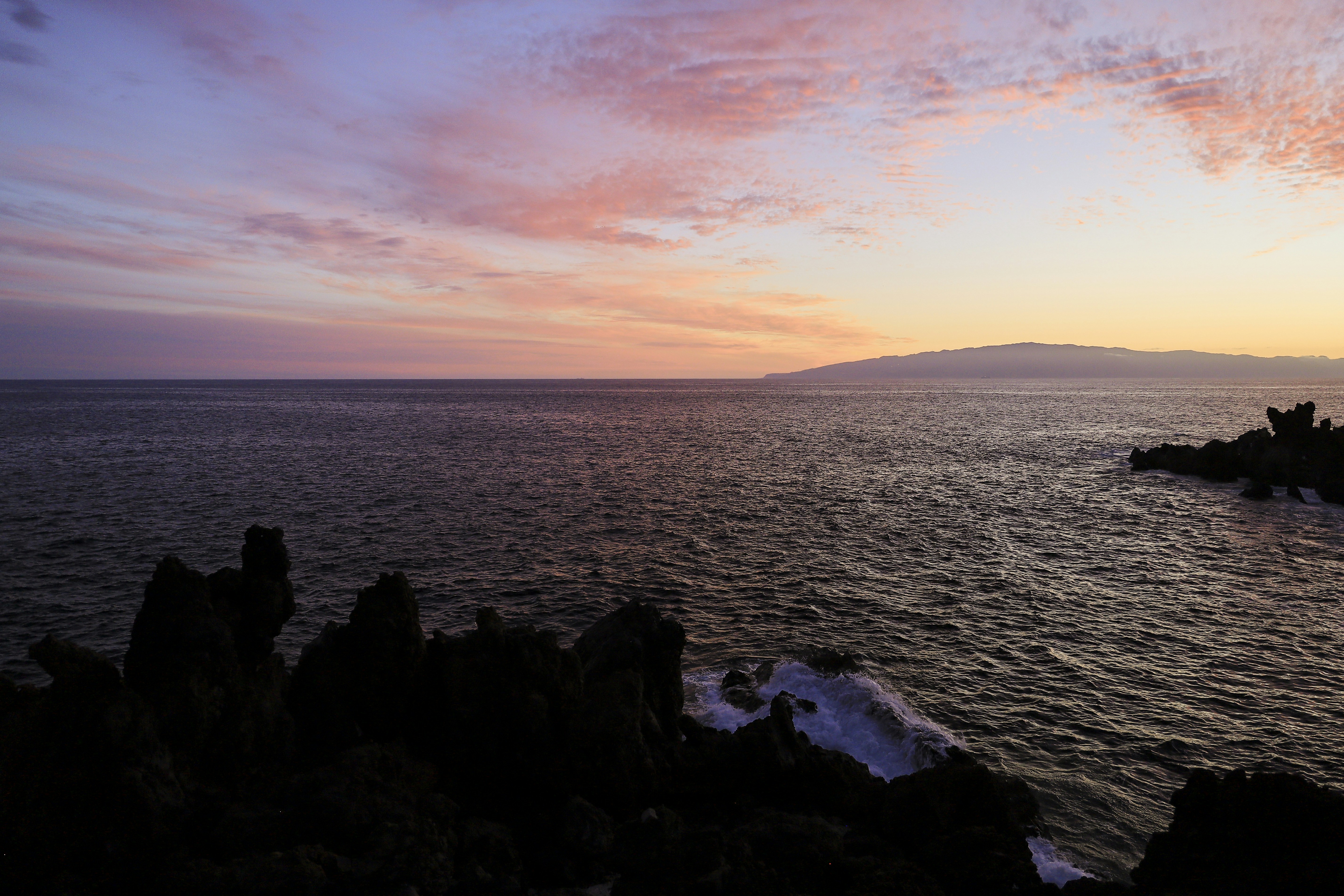 a sunset over a body of water with rocks in the foreground