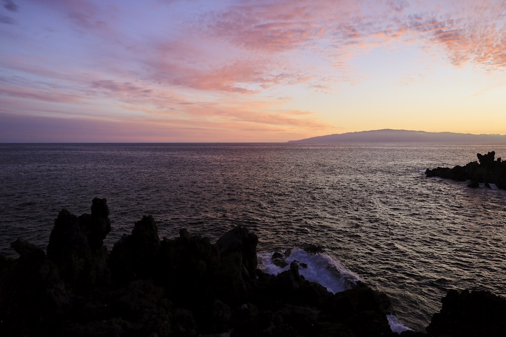 a sunset over a body of water with rocks in the foreground