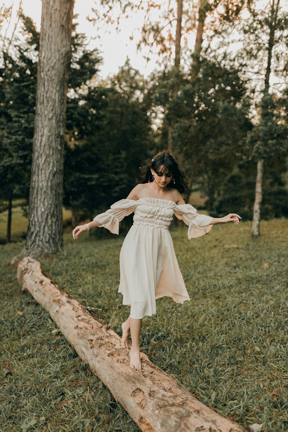 a girl in a white dress is balancing on a log