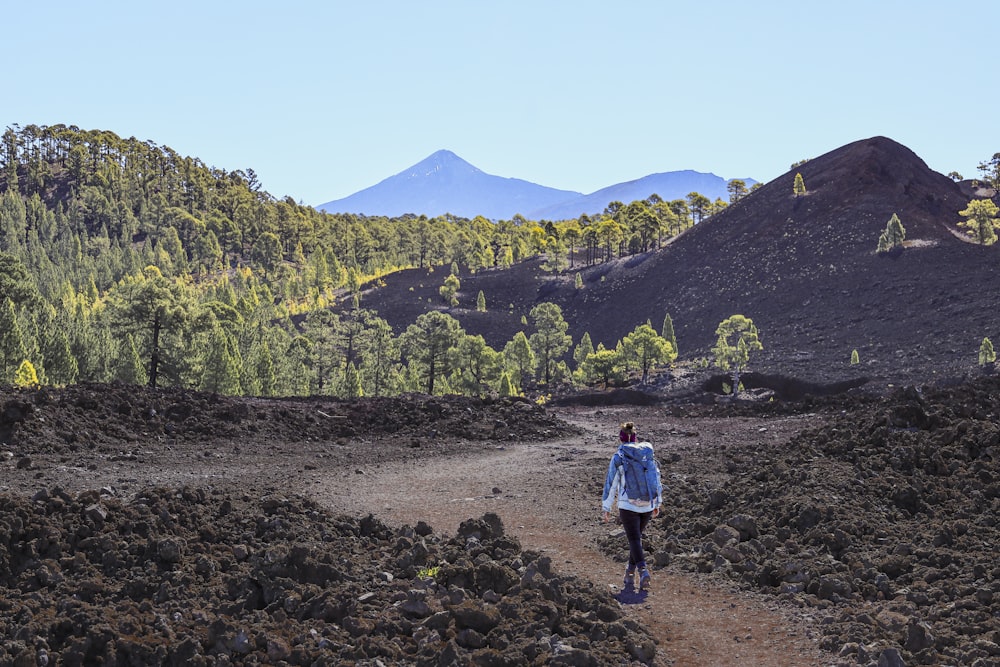 a woman walking down a dirt path in the mountains