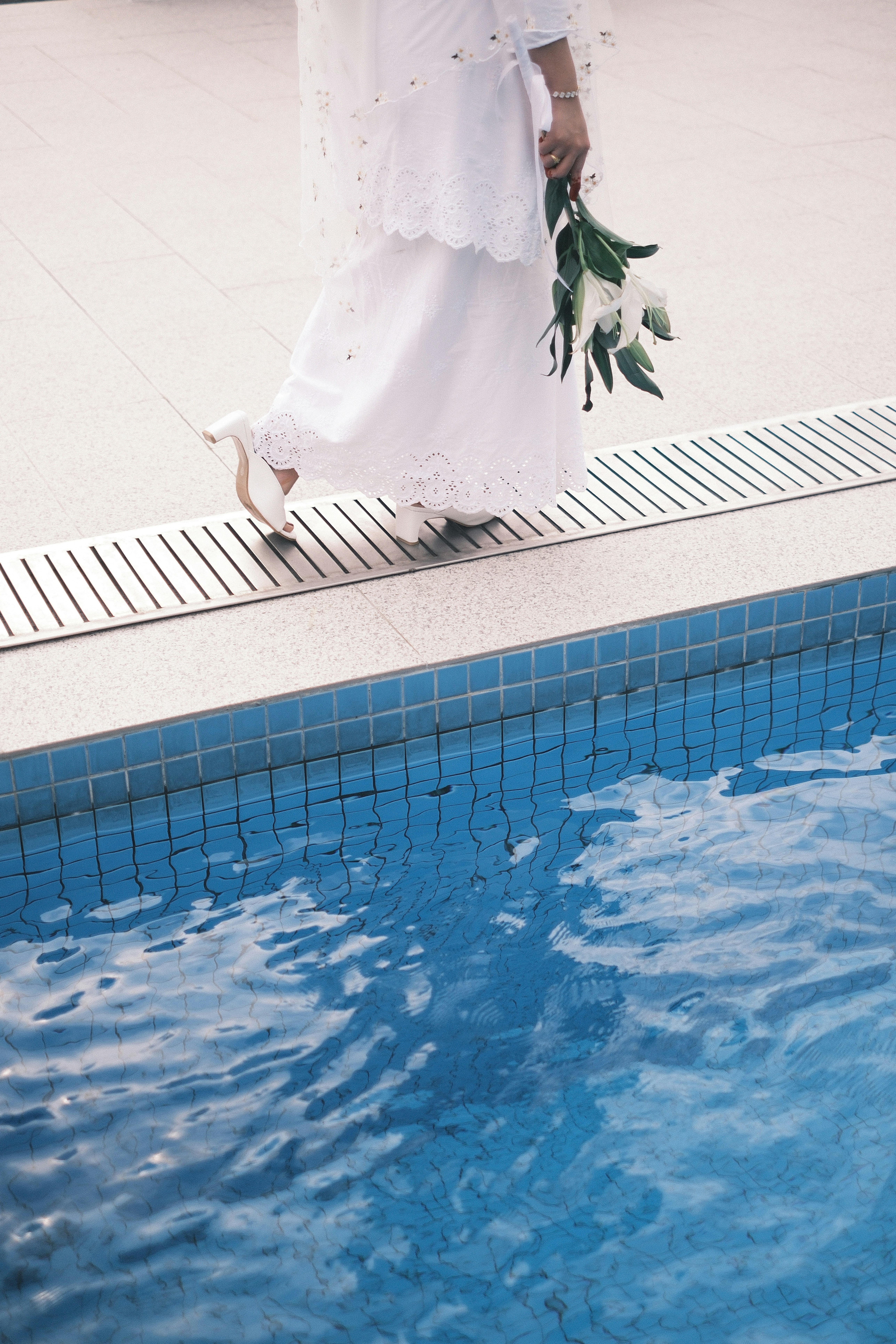 a woman in a white dress holding a bouquet of flowers next to a swimming pool