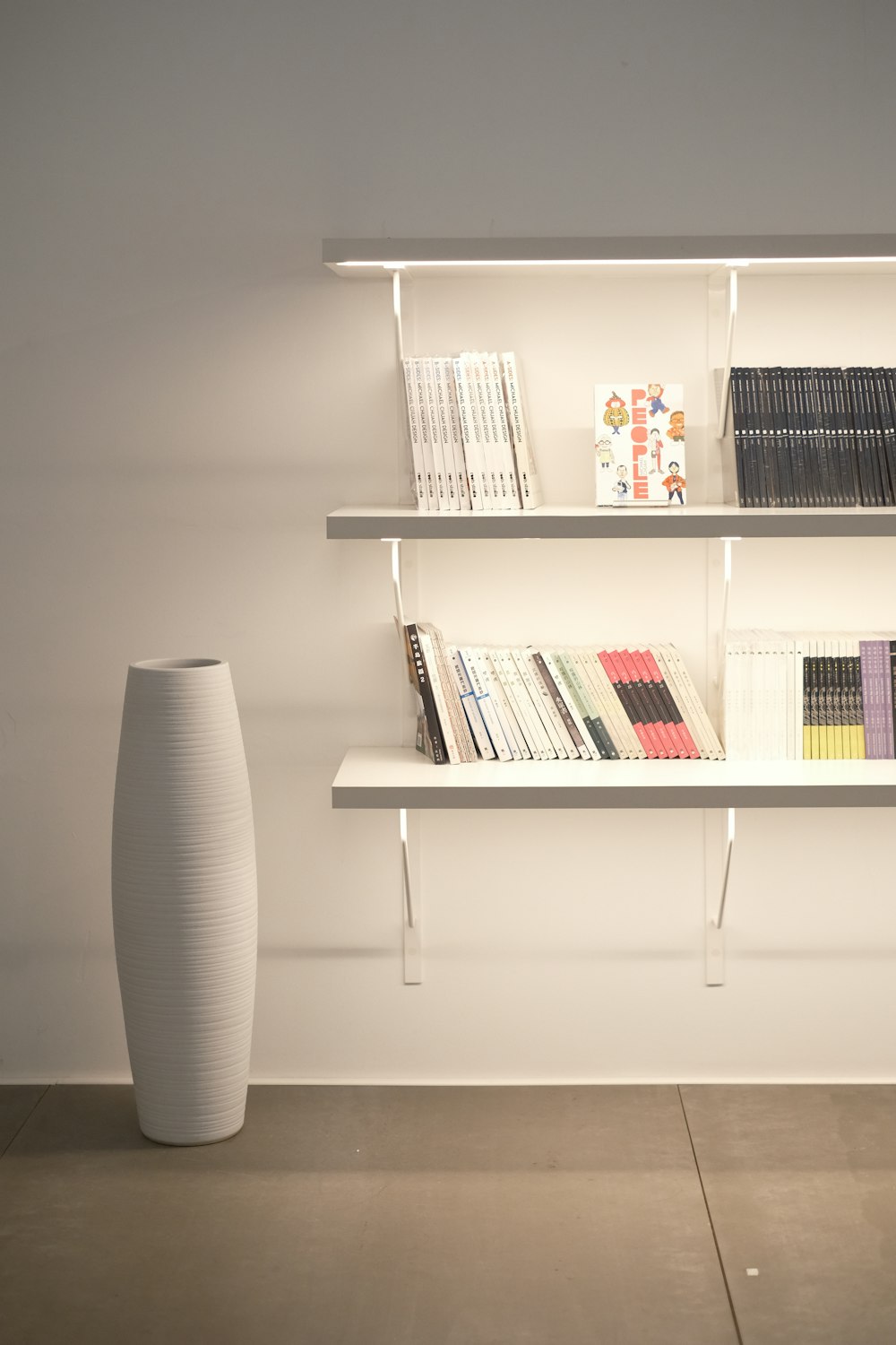 a white vase sitting next to a white shelf filled with books