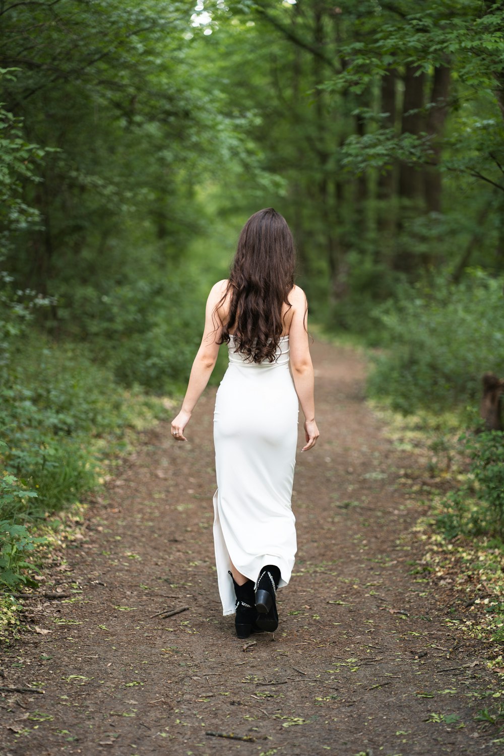 a woman in a white dress walking down a dirt road