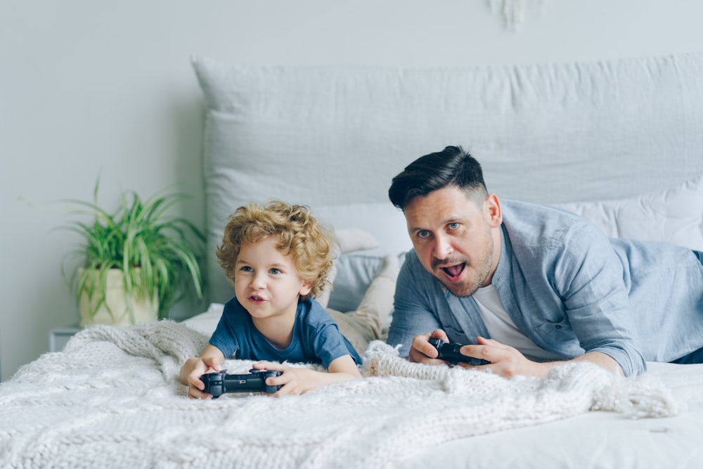 a man and a child laying on a bed playing a video game