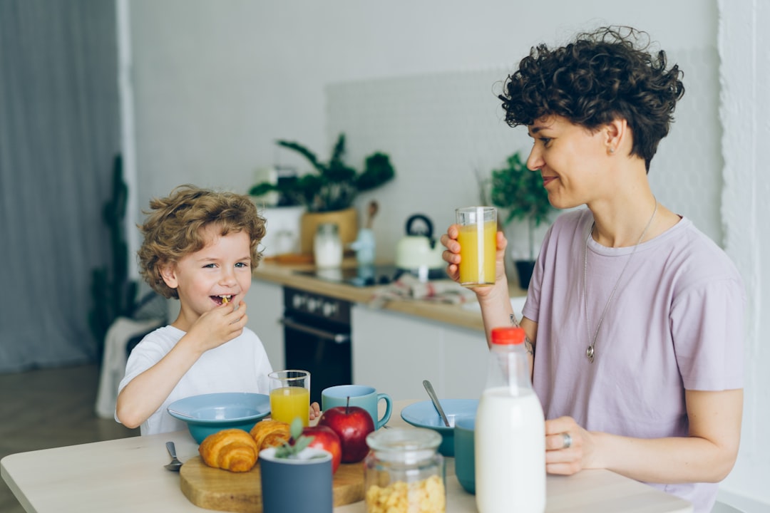 Young woman drinking orange juice while son eating cereal at table in kitchen
