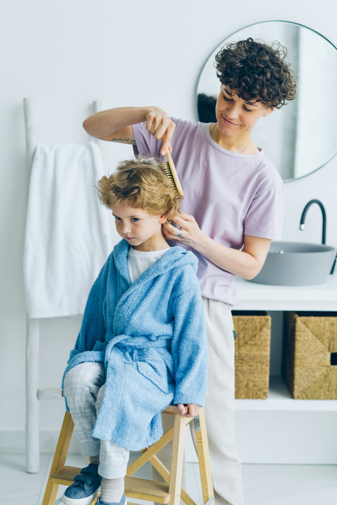 Young woman in pajamas combing small boys hair in bathroom smiling