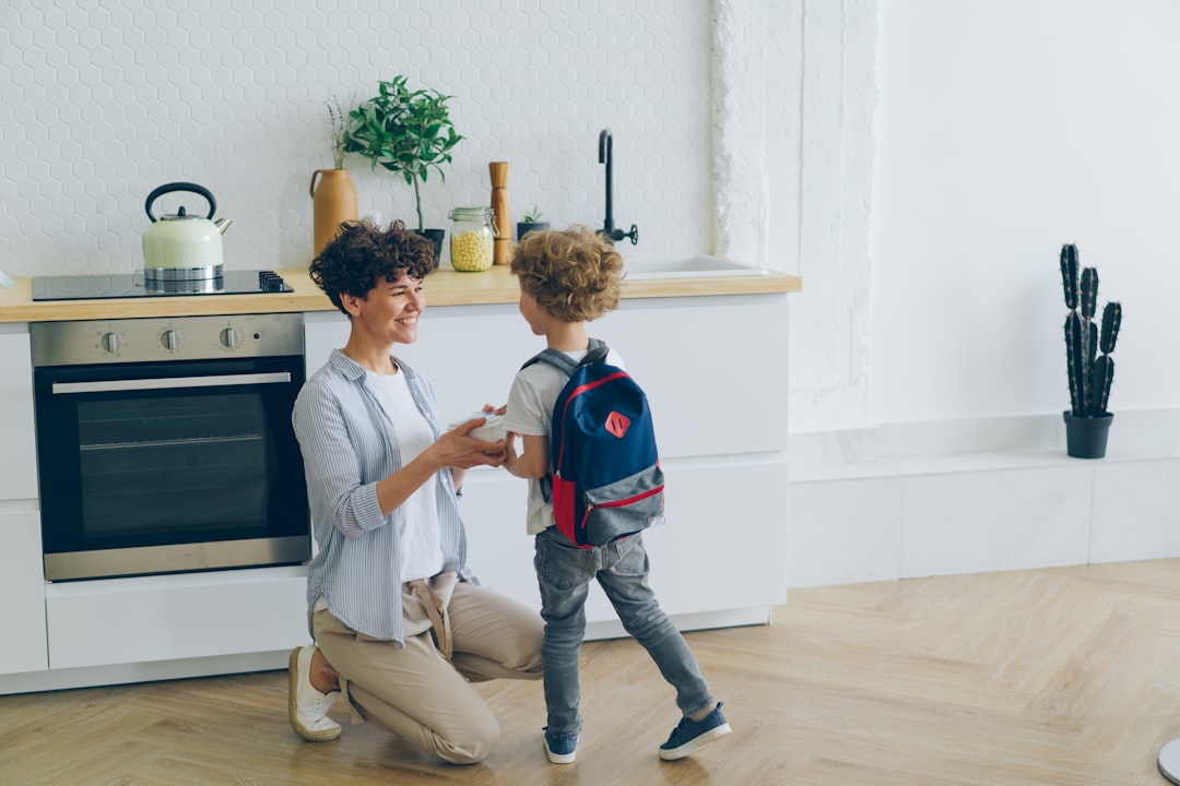 Loving mother giving lunch box to boy with school bag in kitchen smiling