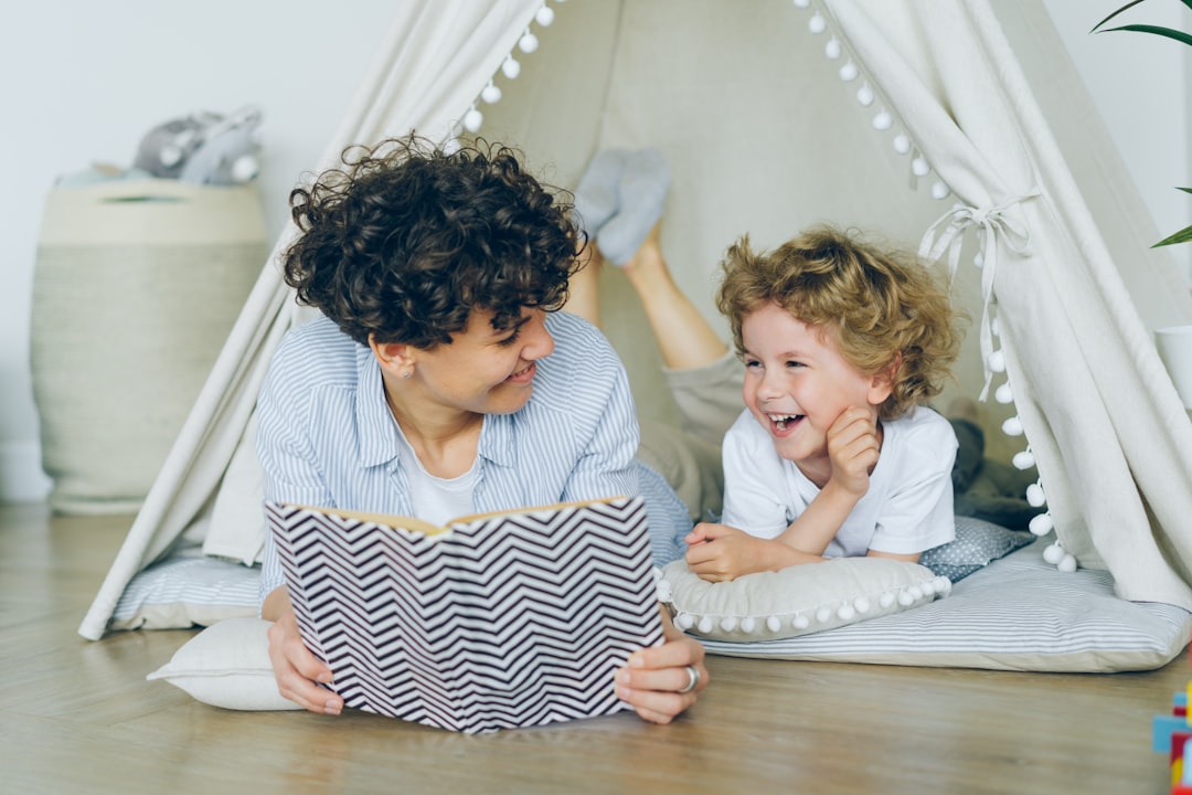 Loving mother reading book to cute child lying on floor in cosy tent indoors