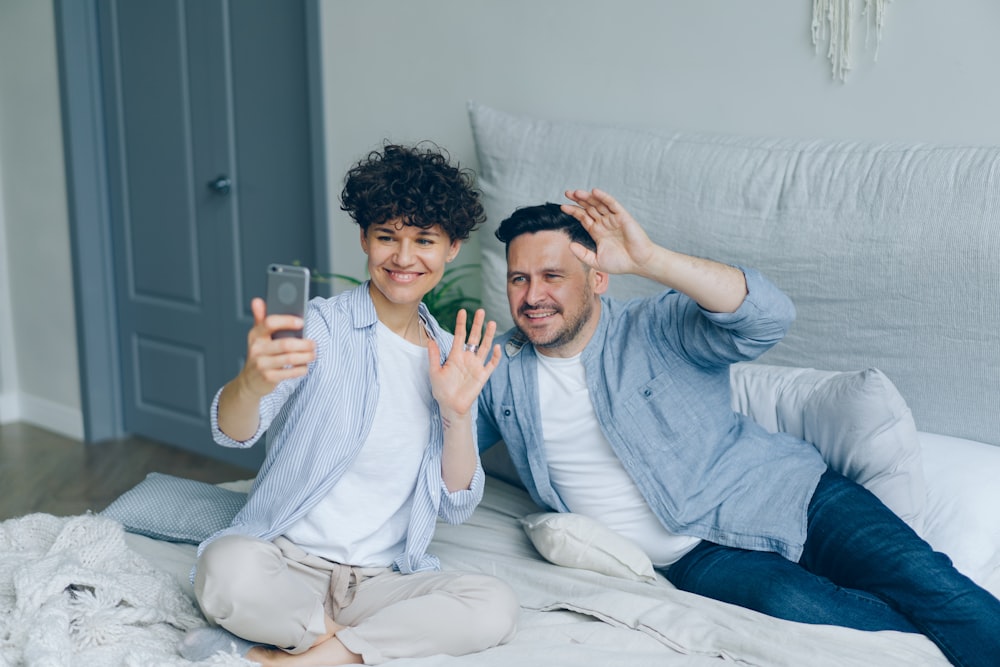 a man and woman sitting on a bed taking a selfie