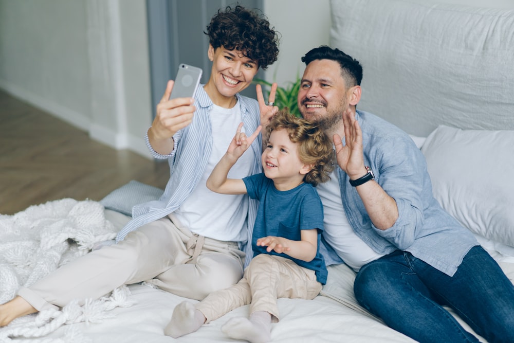 a man, woman and child sitting on a bed taking a selfie