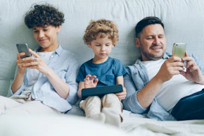 a man, woman and child sitting on a couch looking at their cell phones