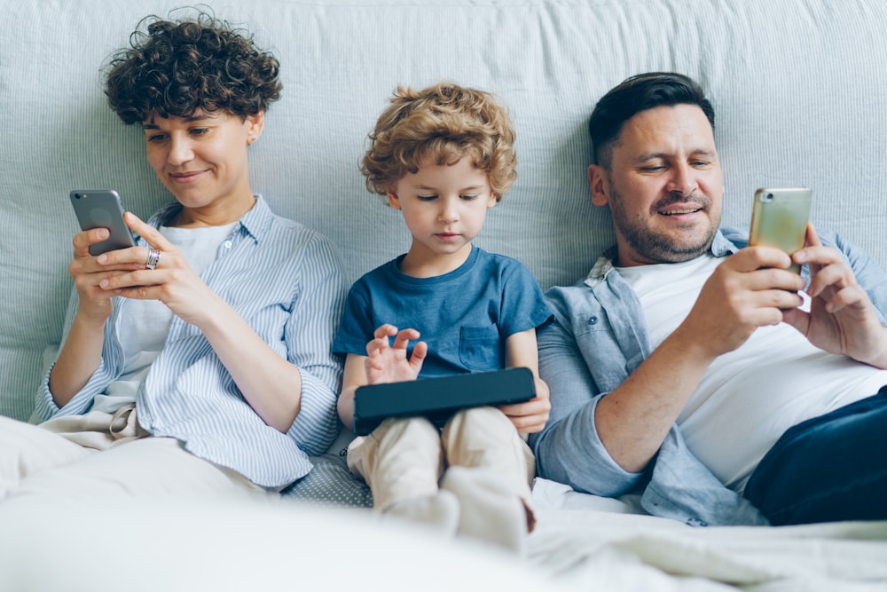 a man, woman and child sitting on a couch looking at their cell phones