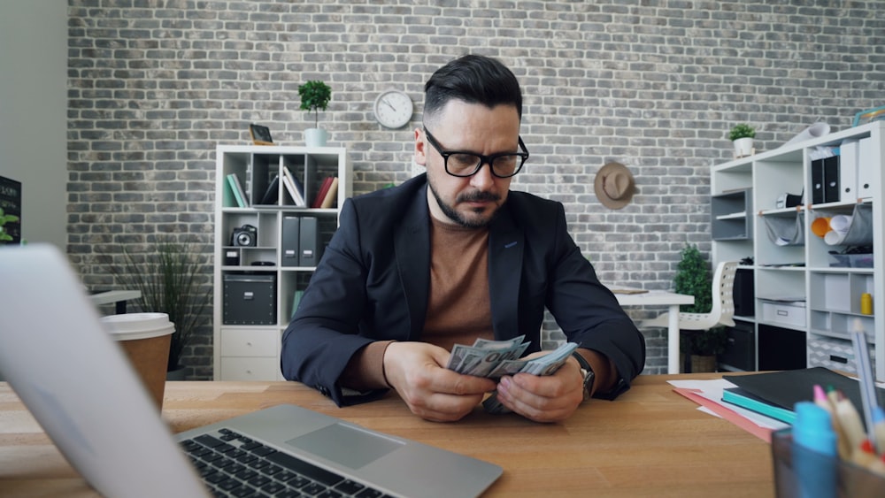 a man sitting at a table with a laptop and money