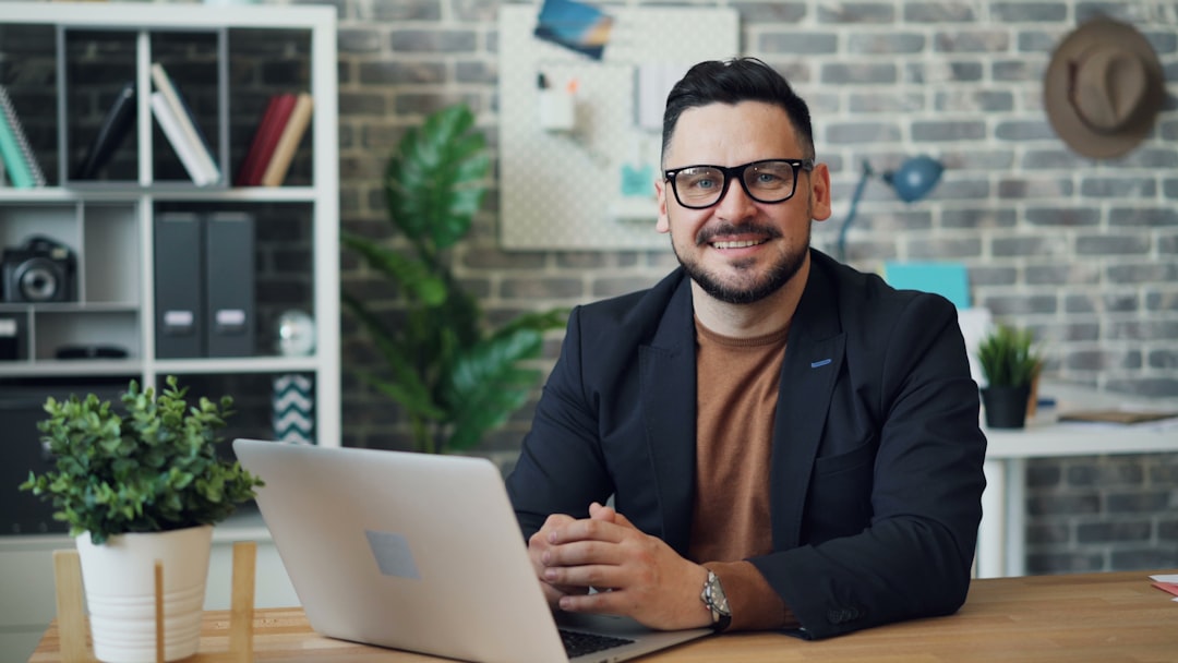 a man sitting at a table with a laptop, portrait of attractive guy using laptop then looking at camera smiling