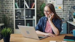 a woman talking on a cell phone while using a laptop
