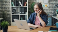 a woman talking on a cell phone while using a laptop