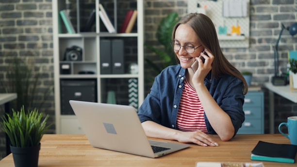 a woman talking on a cell phone while using a laptop