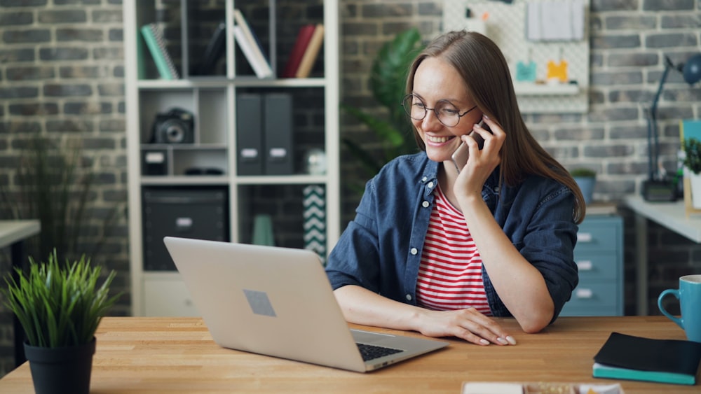 a woman talking on a cell phone while using a laptop