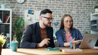 a man and a woman sitting at a table looking at a laptop