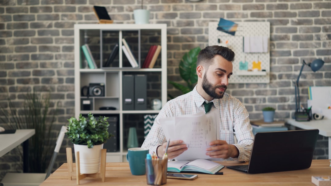 a man sitting at a desk with a laptop and papers, Unhappy businessman looking at papers laptop screen