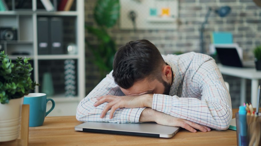 A man resting his head on his desk, overwhelmed