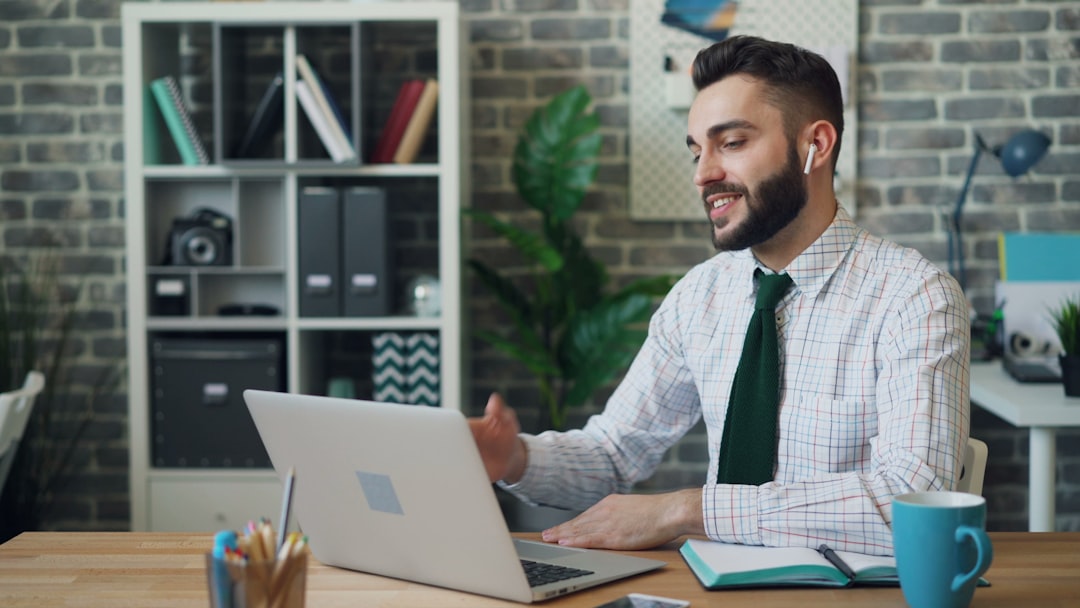 Joyful office worker making video call with laptop wireless earphones at work