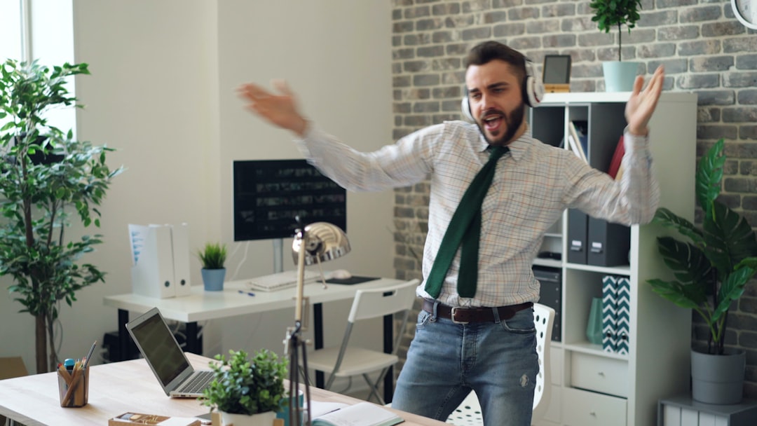 Handsome young man dancing listening to music in headphones in modern office