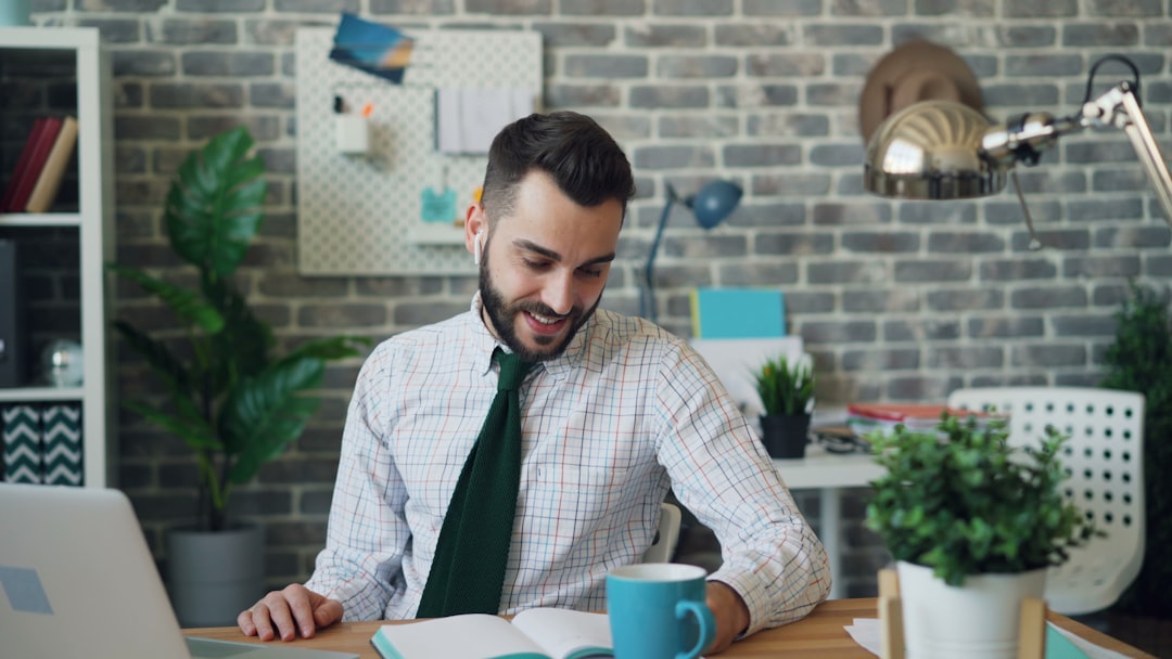 Happy manager communicating with laptop and earphones writing in notebook