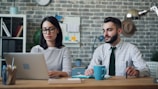 a man and a woman sitting at a table with a laptop