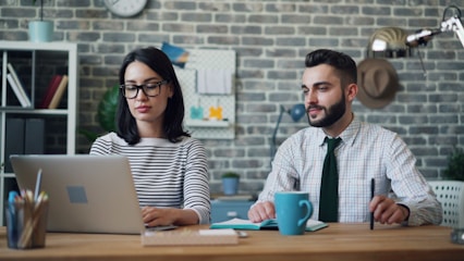 a man and a woman sitting at a table with a laptop