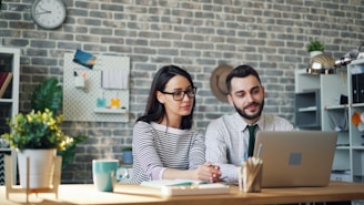 a man and woman sitting at a table looking at a laptop