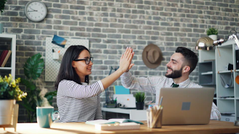 a man and a woman high fiving each other in front of a laptop