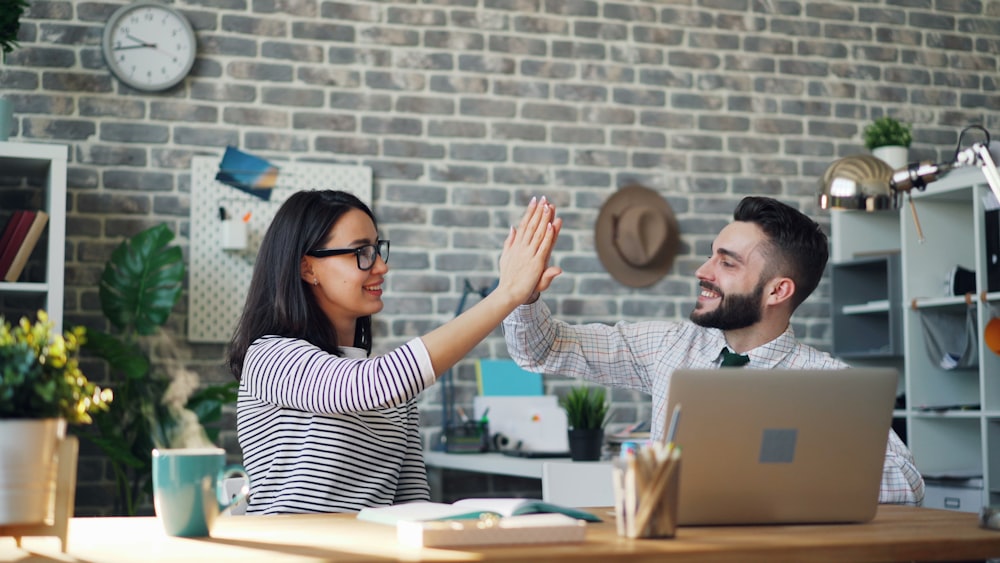 a man and a woman high fiving each other in front of a laptop