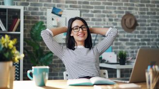 a woman sitting at a desk with her hands behind her head