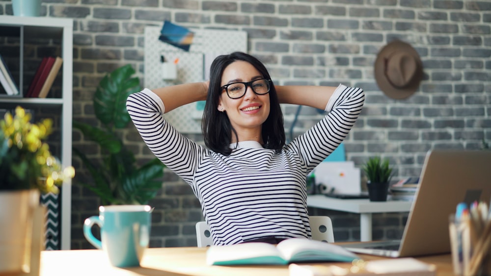 a woman sitting at a desk with her hands behind her head