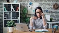 a woman sitting at a desk talking on a cell phone