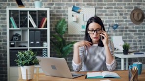 a woman sitting at a desk talking on a cell phone