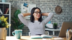 a woman sitting at a desk with her hands behind her head