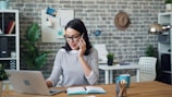 a woman talking on a cell phone while using a laptop