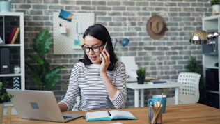a woman talking on a cell phone while using a laptop