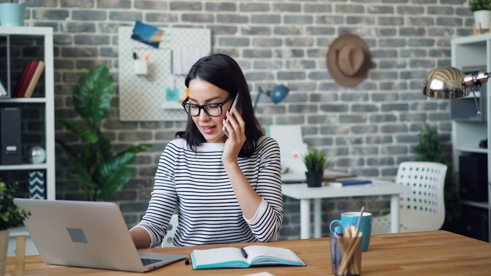 a woman talking on a cell phone while using a laptop