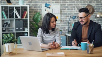 a man and a woman sitting at a table looking at a laptop