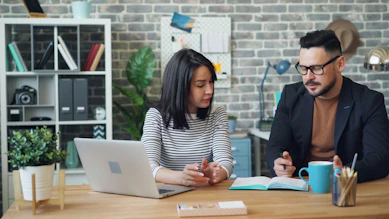 a man and a woman sitting at a table looking at a laptop