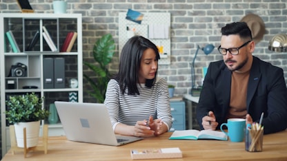 a man and a woman sitting at a table looking at a laptop