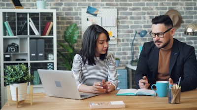 a man and a woman sitting at a table looking at a laptop