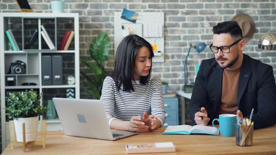 a man and a woman sitting at a table looking at a laptop