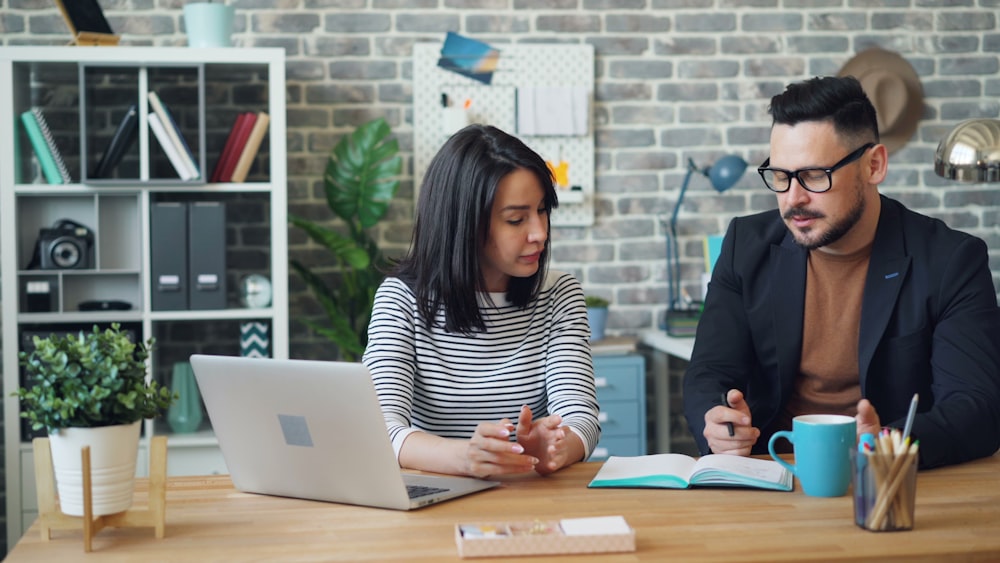 a man and a woman sitting at a table looking at a laptop