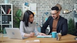a man and a woman sitting at a table looking at a laptop