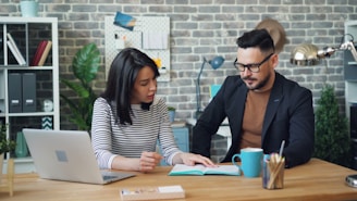 a man and a woman sitting at a table looking at a laptop